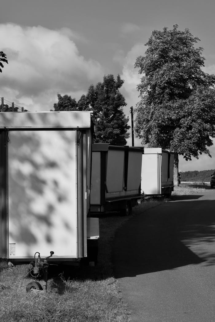 our-story Monochrome image of trailers lined along a rural road under a bright sky.